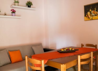 Modern dining room with a wooden table, orange runner, grey sofa, and minimalist wall shelves.