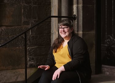 Laura is sitting on stone steps and smiling just away from the camera in direct sunlight