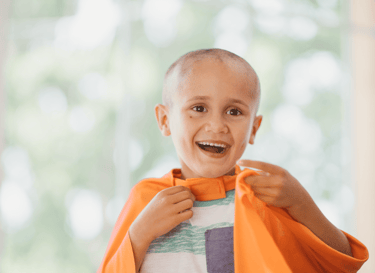 Criança que está passando pelo tratamento contra o câncer brincando com uma capa laranja