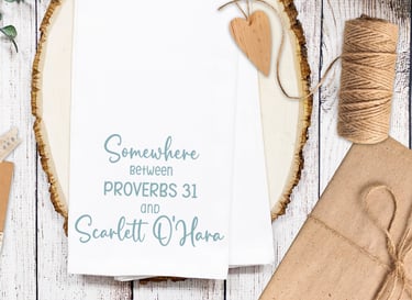 Kitchen towel printed with the saying "Somewhere between Provers 31 and Scarlett O'Hara" for Christian mom woman gift