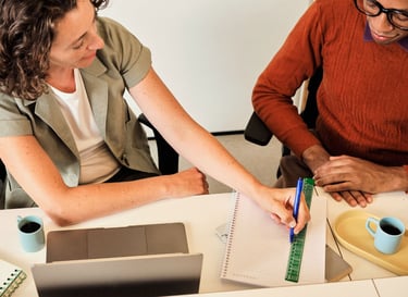 A woman writes in a notebook with a ruler during a professional meeting with a colleague.