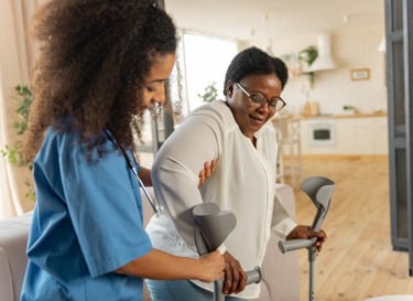 A woman using crutches stands beside another woman using a walker, both smiling in a supportive envi