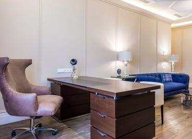 Modern home office featuring a dark wood executive desk, leather wingback chair, and blue velvet sofa.