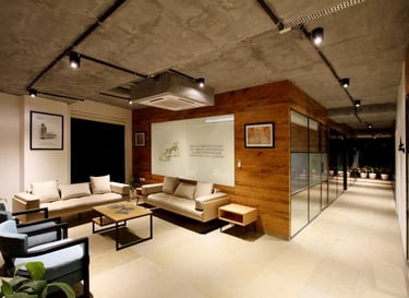 Modern office waiting area with industrial concrete ceilings, wood paneling, and comfortable sofas.