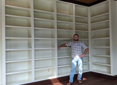 Custom built-in white bookshelves in a home library with wood floors and a cedar ceiling.
