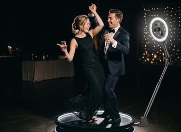 A happy couple dancing on a 360 photo booth platform at a formal event with a ring light camera.