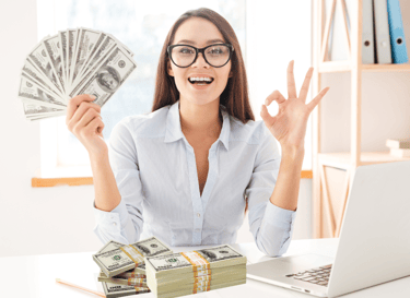 a woman sitting at a desk with a laptop and holding up a stack of money