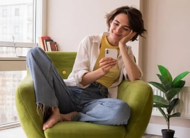 Femme assise confortablement en tailleur, tenant son téléphone et souriant doucement.