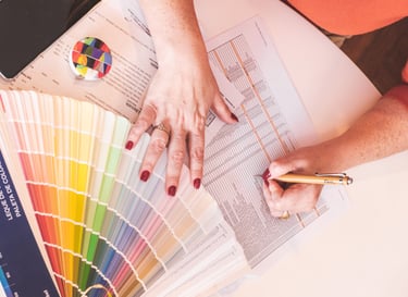 Interior designer choosing paint colors from a fan deck swatch while writing on a technical document.