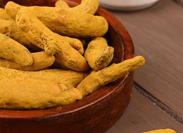Dried whole turmeric roots in a small wooden bowl on a rustic table.