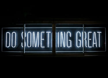 A neon sign with white lettering that reads "DO SOMETHING GREAT" is illuminated against black color