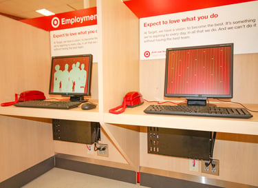 Two retail employment kiosks with computers, red telephones, and professionally managed network equipment installed below.