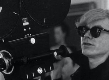 Andy Warhol segurando uma câmera de filme antiga, usando óculos escuros preta