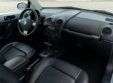 Interior do Volkswagen New Beetle com painel, volante e bancos em couro preto.