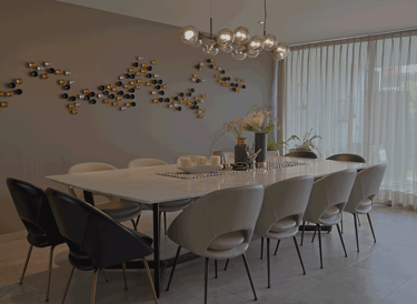 Comedor amplio con mesa de mármol, sillas curvas beige y decoración mural artística | KARÄNA