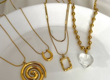 Colección de collares de oro con diseños de espiral, herradura y corazón de cristal en placa blanca