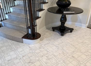 Elegant foyer featuring marble tile flooring, a carpeted staircase with wood banister, and a round accent table.