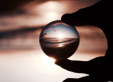 Des doigts tenant une boule de cristal reflétant avec clarté un coucher de soleil sur la mer