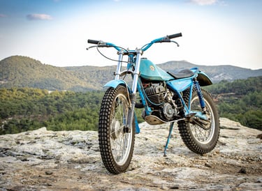 a blue Bultaco motorcycle parked on a rocky mountain