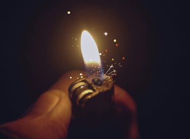 A hand holding a lit cigarette lighter at night