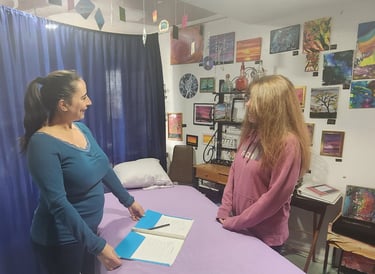 A Reiki therapist consults with a client in a studio decorated with colorful art and paintings.