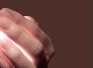 Eine Hand mit die etwas Helles im Inneren umschließt was durch die Finger scheint