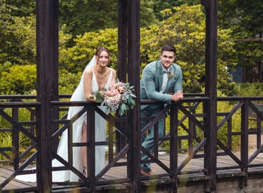 Brautpaar lehnt entspannt an einer Holzbrücke im Grünen. Hochzeitsportrait von Just Perspectives.