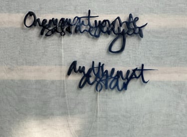 Two lines of semi-abstract text, made in glass and joined by a silver rope chain.