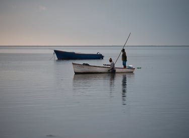 Fishermen at Petite Case Noyale on a traditional wooden boat in calm waters of Mauritius, reflecting the serene early morning