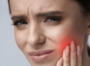 Mulher com a mão no rosto ilustrando sintomas de bruxismo avaliados por dentista na Lapa PR.