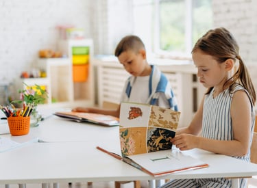 A girl and a boy sit at table reading.