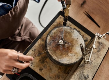 Joyero con un soplete de gas para soldar un anillo de plata en un bloque de soldadura en un taller.