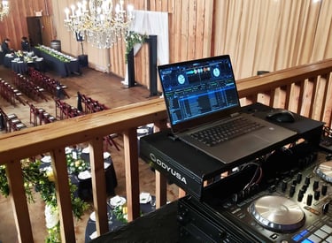 a dj booth with a laptop overlooking a wedding ceremony space from the balcony