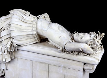 Small ceramic sculpture of a woman in a fancy skirt on exam table with bandages and a drain for breast reconstruction.