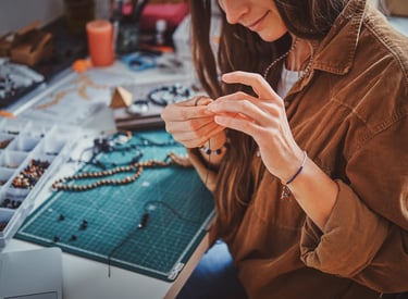 Un joyero elabora un collar hecho a mano con cuentas en un escritorio de taller con herramientas.