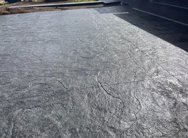 Dark gray stamped concrete driveway with a textured slate finish for a modern home exterior.