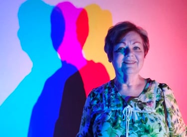 Photo of Debbie with multicolor lights and shadows cast upon the blank wall beside her.