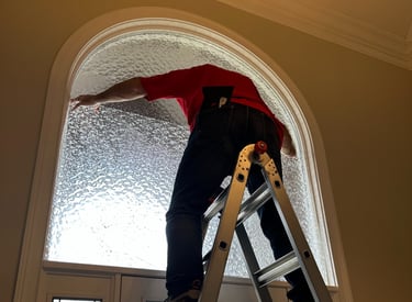 Man on ladder tinting foyer window with decorative film