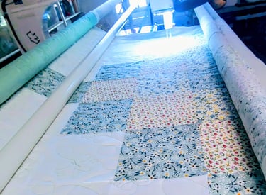 Longarm quilting machine stitching floral and butterfly patterns on a colorful patchwork quilt top.