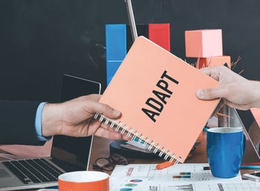 Um caderno tipo manual escrito Adapt é passado de mão em mão em uma mesa de escritório.