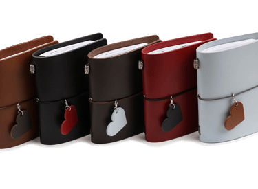 a group of four leather bound journals with a heart shaped leather tags