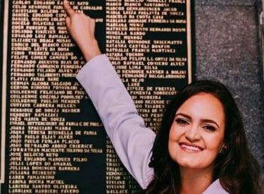 Dra Bruna Melchior de jaleco branco apontando seu nome em placa de metal do Hospital das Clinicas da USP de Ribeirao Preto