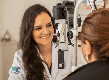 Dra Bruna Melchior de jaleco branco examinando paciente em aparelho de oftalmologia