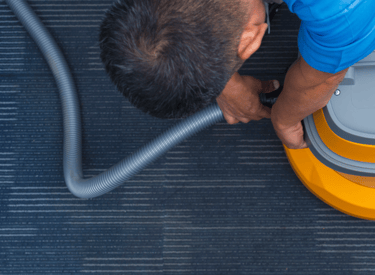 a man in a blue shirt connecting a hose to a carpet cleaning machine 