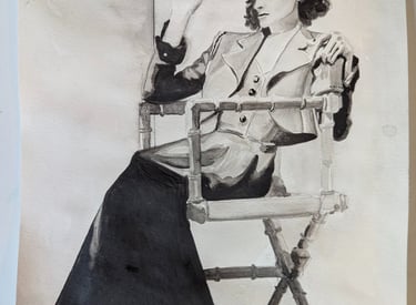 A graphite drawing of a classic 30s photo of Katherine Hepburn sitting in a director's chair rendered by Kathy LaFollett.