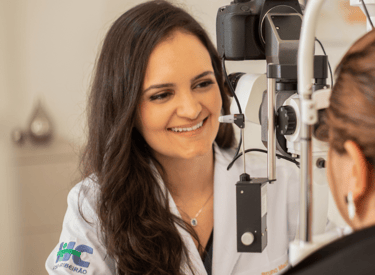 Dra Bruna Melchior de jaleco branco examinando paciente em aparelho de oftalmologia