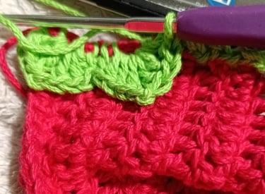 Primer plano de un proyecto de crochet de fresa roja y verde hecho a mano con un ganchillo morado.