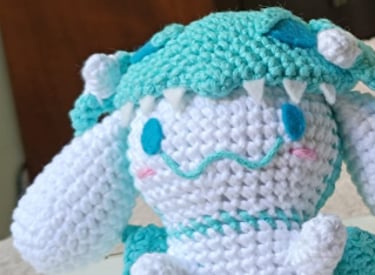 Dos peluches Cinnamoroll tejidos a mano, uno de ellos con un disfraz de dragón verde azulado.