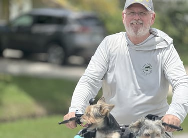 Robert smiling while riding a bicycle with two dogs in a basket