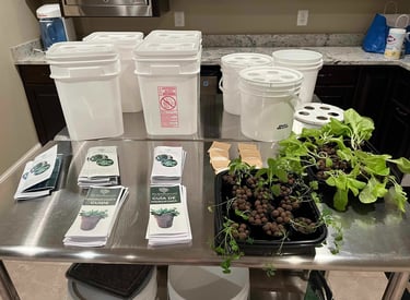 Hydroponic grow buckets, brochures, and lettuce seedlings on a table